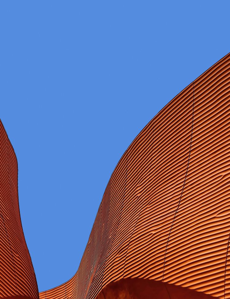 The B&B Expo Milano in Milanese, Italy. A sparse orange-copper coloured building with clear blue sky in the background.