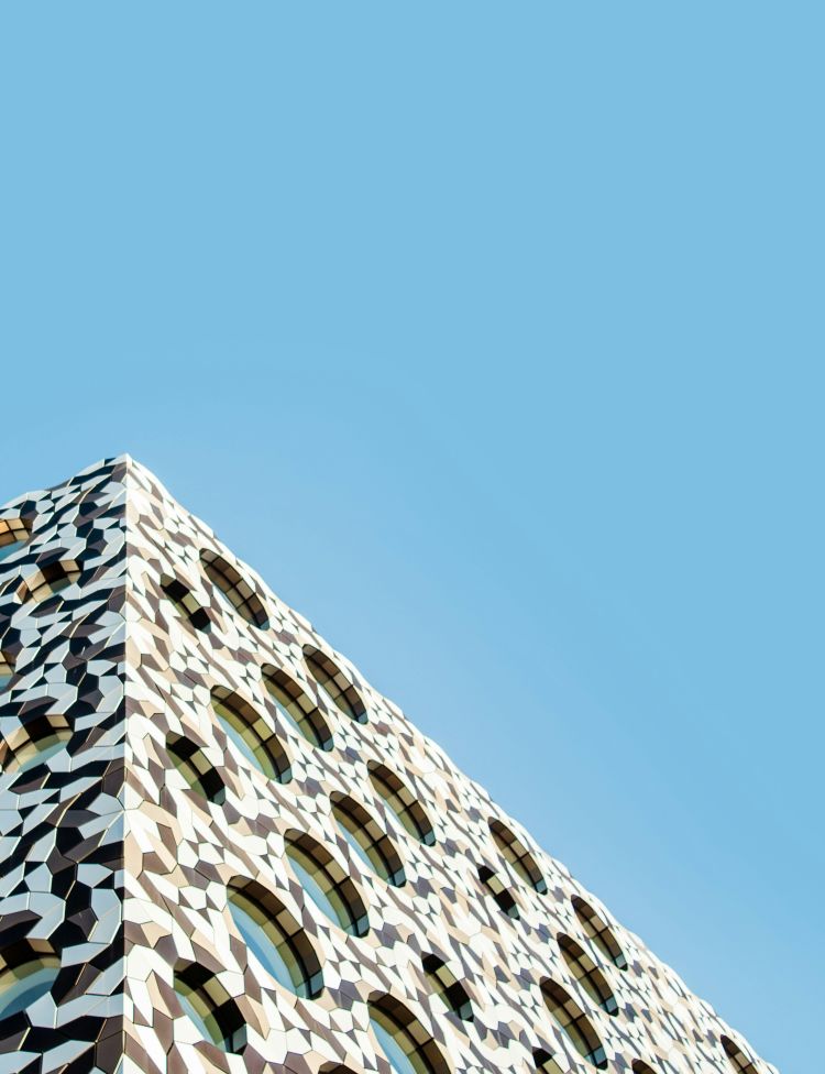 A patterned modern building with portholes in Greenwich, set against blue sky.