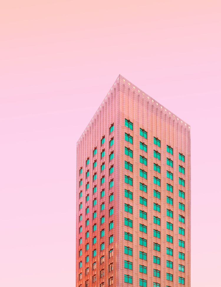 A thin orange tinted skyscraper with green-tinted windows set against a gradiented sky.